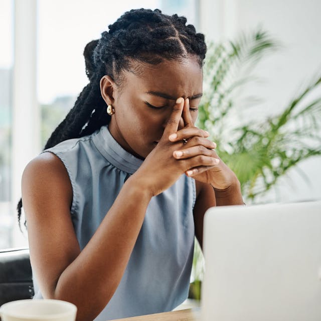 Stressed African American woman feeling overwhelmed at work, emphasising the negative impacts of people-pleasing in the workplace.